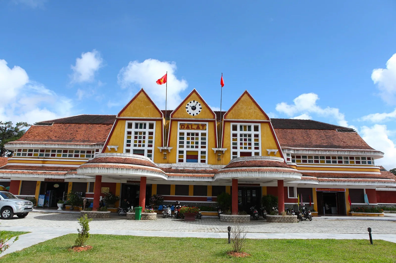 Mặt tiền nhà ga xe lửa Đà Lạt cổ kính với các mái tam giác và tháp đồng hồ trung tâm dưới trời xanh.