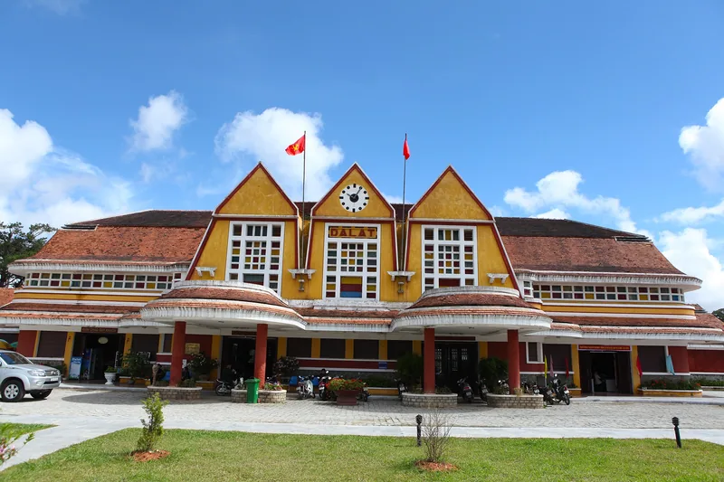 Mặt tiền nhà ga xe lửa Đà Lạt cổ kính với các mái tam giác và tháp đồng hồ trung tâm dưới trời xanh.